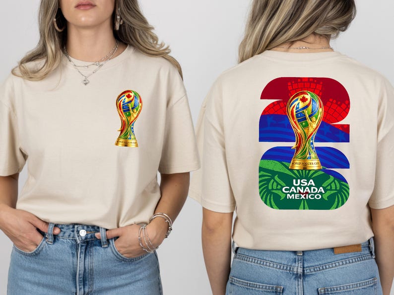 May include: Beige t-shirt featuring a colorful trophy graphic on the front and back. The front has a small trophy, while the back displays a larger trophy design with the text "USA CANADA MEXICO". The shirt is made of a soft material.