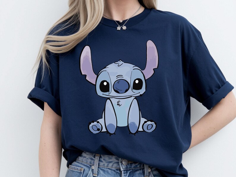 Puede incluir: Camiseta azul marino con una ilustraci&oacute;n de dibujos animados de Stitch, una criatura extraterrestre azul con orejas grandes y ojos grandes. El gr&aacute;fico est&aacute; centrado en la parte delantera de la camiseta. La camiseta es de material suave.
