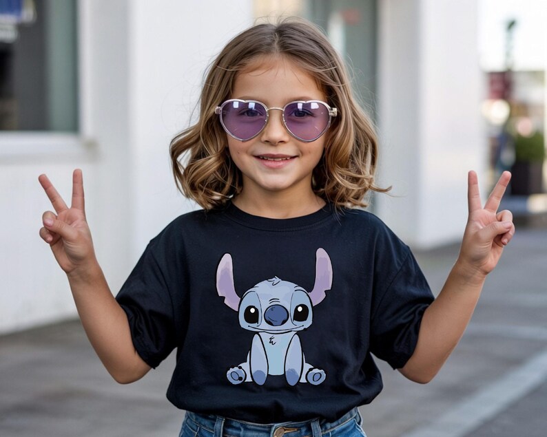Puede incluir: Una ni&ntilde;a lleva gafas de sol moradas en forma de coraz&oacute;n y una camiseta negra con un personaje de dibujos animados. La ni&ntilde;a sonr&iacute;e y hace el signo de la paz con ambas manos. La camiseta tiene un dise&ntilde;o azul y morado.