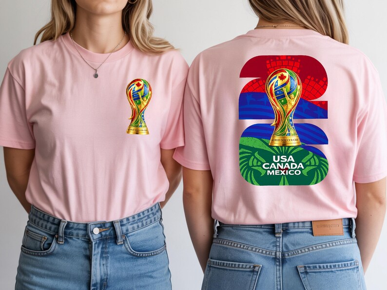 May include: Two pink t-shirts with a colorful graphic of a trophy on the front and back. The back of the shirt has the number 26, a trophy graphic, and the text "USA CANADA MEXICO". The shirts are worn with blue jeans.