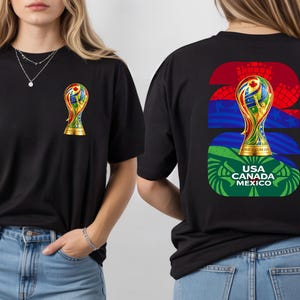 May include: Black t-shirt featuring a colorful trophy design on the front and back. The back of the shirt displays the number 22, a trophy graphic, and the text "USA CANADA MEXICO". The front of the shirt has a smaller trophy graphic.