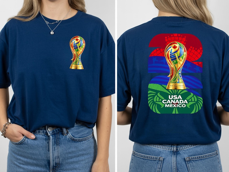 May include: Navy blue t-shirt featuring a colorful trophy design on the front and back. The front displays a small trophy, while the back showcases a larger trophy with the text "USA CANADA MEXICO". The design incorporates flags and the number "26".