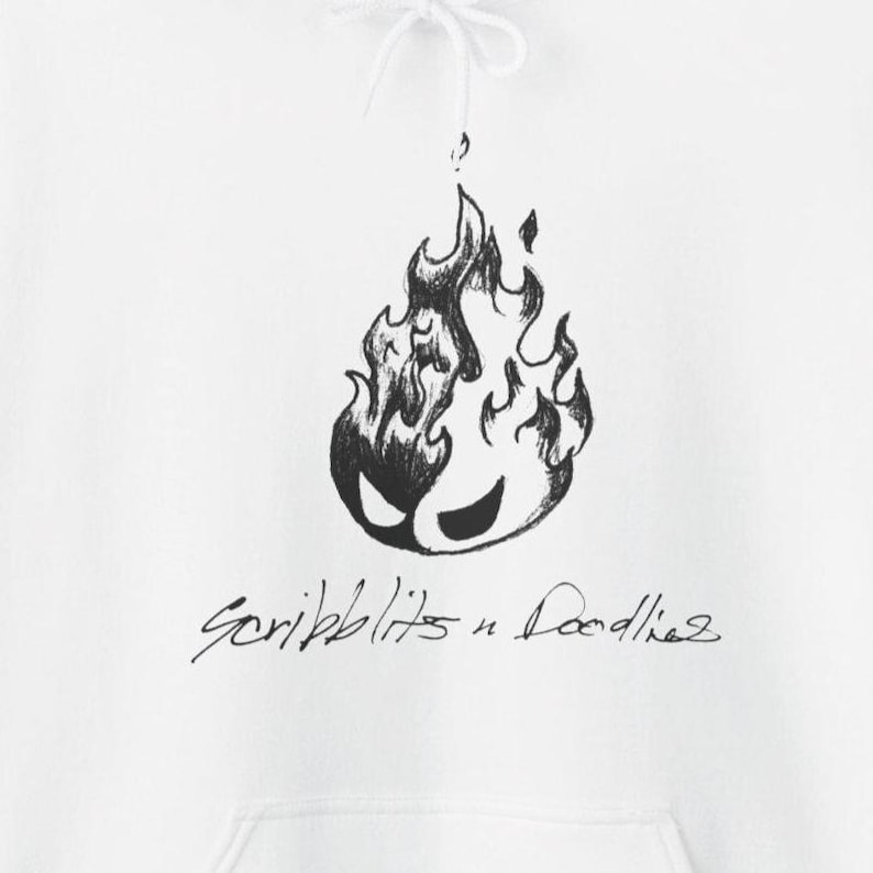 May include: White hoodie with a black and white flame design with a face. The cursive text below reads "Scribblits n Doodles". The hoodie has a drawstring and a front pocket, typical of this style of garment.