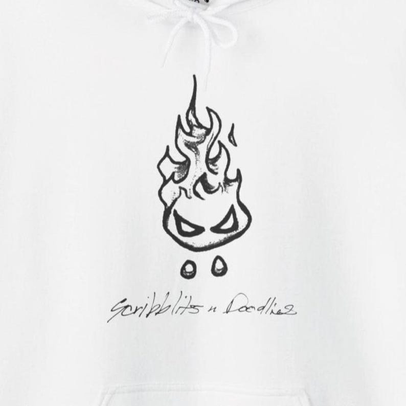 May include: White hoodie with a black doodle of a flame with eyes and two dots beneath. The cursive text "Scribblits n Doodles" is below the flame design. The hoodie has a drawstring hood.