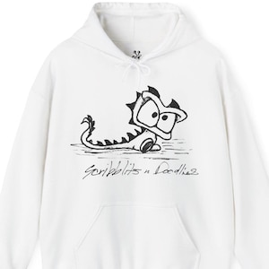 Könnte beinhalten: Weißer Kapuzenpullover mit einem schwarzen Cartoon-Drachen-Motiv. Der Drache hat große Augen und einen stacheligen Rücken. Der Text "Scribblits n Doodles" steht darunter. Der Hoodie hat eine Kapuze mit Kordelzug und eine Vordertasche.