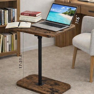 May include: A brown laptop table with a black metal support. The tabletop is 11.8 inches wide and 11.5 inches deep. The base is 15.7 inches wide, and the table is 17.3 inches tall. A laptop, books, and a notebook are on the table.