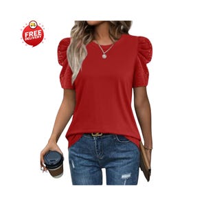 May include: A red short-sleeved top with lace detailing on the sleeves. The top is paired with blue jeans and a gold belt. A coffee cup is held in the left hand. The top has a round neckline.