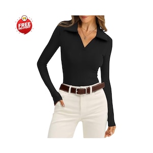 May include: A black long-sleeve shirt with a collared neckline. The shirt has a V-neck design and thumb holes at the cuffs. A brown belt with a silver buckle is worn with white pants. The image includes a "Free Delivery" graphic.