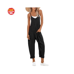 Könnte beinhalten: Schwarzer Jumpsuit mit Spaghettiträgern und großen Vordertaschen. Der Jumpsuit wird mit einem weißen Oberteil darunter und weißen Slip-On-Schuhen kombiniert. Auf dem Kopf wird ein Strohhut getragen. Das Bild enthält ein "KOSTENLOSER VERSAND"-Logo.