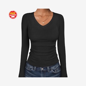 May include: A black long-sleeve V-neck shirt with a ribbed texture. The shirt has a fitted silhouette and is paired with blue jeans. A gold necklace with a cross pendant is visible.