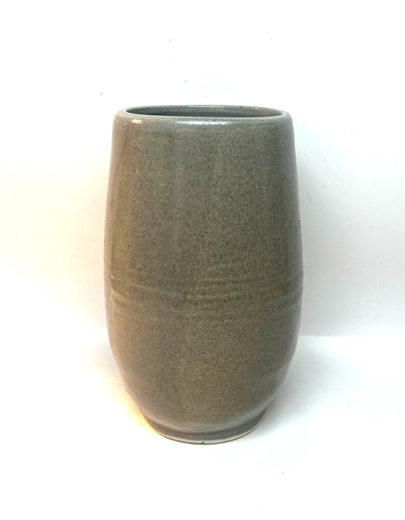 Puede incluir: Un jarr&oacute;n de cer&aacute;mica gris con un cuerpo redondeado y una parte superior ligeramente ensanchada. El jarr&oacute;n tiene una textura moteada y un acabado liso y brillante. El jarr&oacute;n mide unos 20 cm de alto.