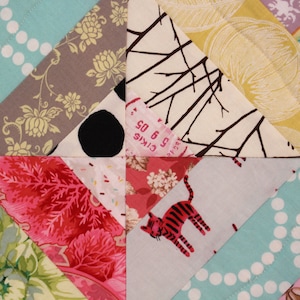 May include: Close-up of a patchwork quilt with various patterned fabrics. The quilt features triangles of teal with white polka dots, floral prints, and a fabric with a red tiger. The quilt has a variety of colors and textures.