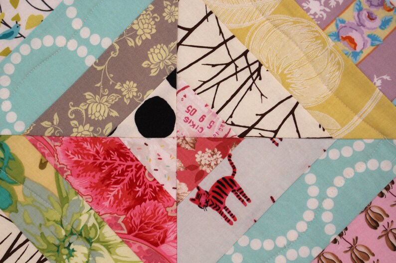 May include: Close-up of a patchwork quilt with various patterned fabrics. The quilt features triangles of teal with white polka dots, floral prints, and a fabric with a red tiger. The quilt has a variety of colors and textures.