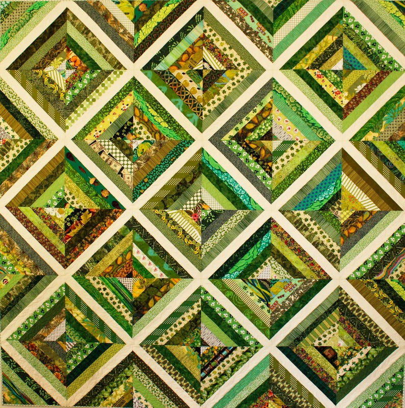 May include: A handmade quilt featuring a patchwork design with various shades of green fabrics. The quilt is composed of square blocks, each divided into diamond shapes with diagonal stripes. The color palette includes olive, lime, and forest green.