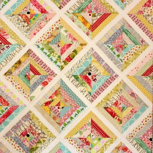 May include: A colorful patchwork quilt with a repeating geometric pattern. The quilt features various fabric strips in shades of pink, yellow, green, and blue, arranged in diagonal lines. White fabric separates the patterned blocks, creating a grid-like design.