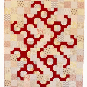 May include: A red geometric pattern quilt with a patchwork design. The quilt is made up of squares of different fabrics in shades of beige, cream, and pink.