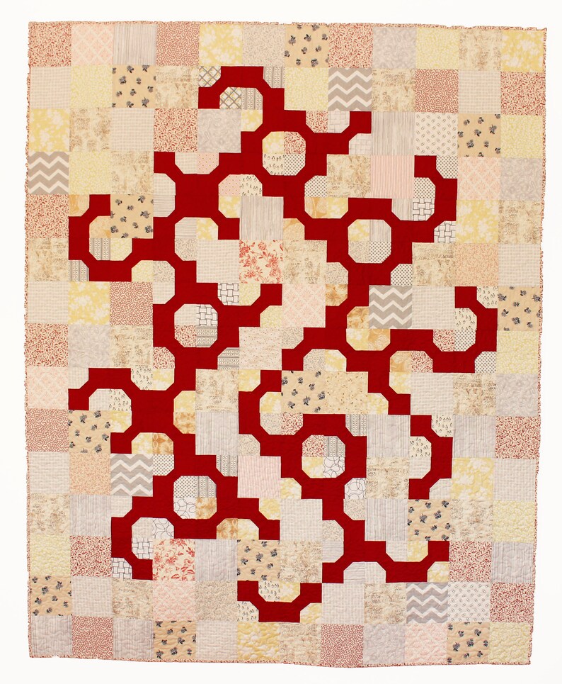 May include: A red geometric pattern quilt with a patchwork design. The quilt is made up of squares of different fabrics in shades of beige, cream, and pink.