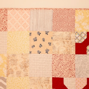 May include: A patchwork quilt with a variety of floral and geometric patterns in shades of red, yellow, and gray. The quilt is made of different fabrics and textures, creating a unique and interesting design.