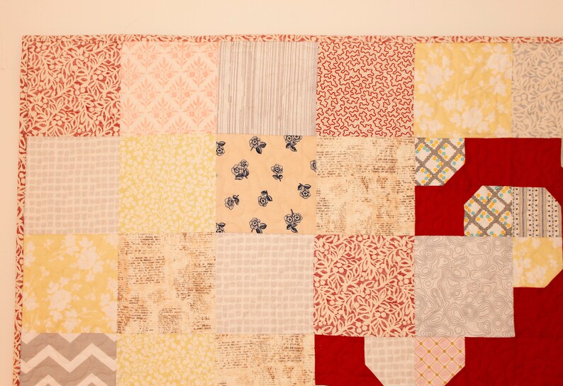May include: A patchwork quilt with a variety of floral and geometric patterns in shades of red, yellow, and gray. The quilt is made of different fabrics and textures, creating a unique and interesting design.