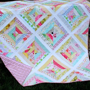 May include: A colorful patchwork quilt with a variety of patterned fabrics in pink, yellow, green, and blue. The quilt features a diamond pattern with white borders and a pink backing. The quilt is made of various fabrics.