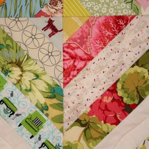 May include: Close-up of a colorful quilt with a diagonal pattern. The quilt features various fabric patterns, including floral, geometric, and cat motifs. The color palette includes green, pink, blue, and yellow.