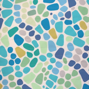 May include: A close-up of a fabric with a pattern of irregular shapes in shades of blue, green, and yellow on a white background. The shapes vary in size and are scattered across the surface. The fabric has a quilted appearance.