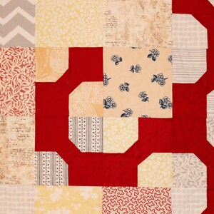 May include: A red, white, and yellow patchwork quilt with a geometric pattern. The quilt is made of different fabrics with various patterns, including floral, geometric, and plaid.