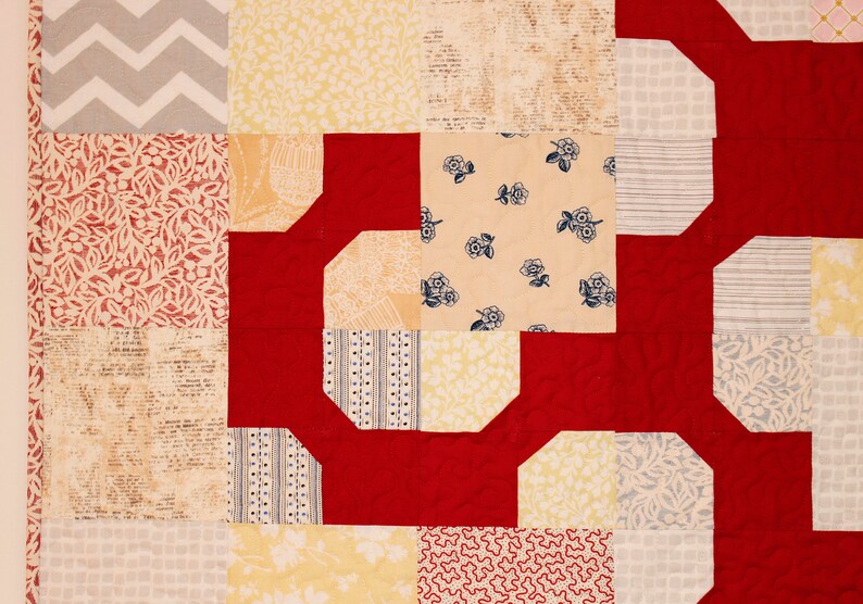 May include: A red, white, and yellow patchwork quilt with a geometric pattern. The quilt is made of different fabrics with various patterns, including floral, geometric, and plaid.