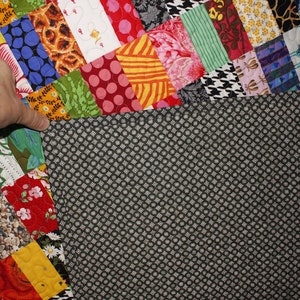 May include: A colorful patchwork quilt with a black and white patterned backing. The quilt is made up of various fabrics with different patterns and colors, including floral, geometric, and animal prints.
