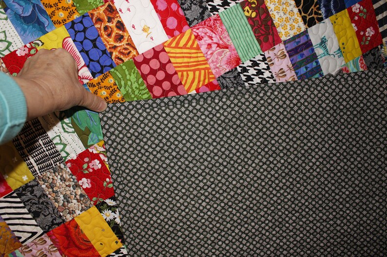 May include: A colorful patchwork quilt with a black and white patterned backing. The quilt is made up of various fabrics with different patterns and colors, including floral, geometric, and animal prints.