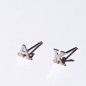 May include: A pair of silver initial earrings, one with the letter "A" and the other with the letter "K".