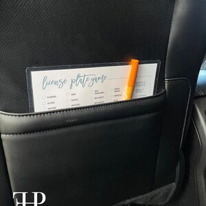 May include: A white card with the text "license plate game" printed on it. The card has a checklist of states with checkboxes next to each state name. A orange marker is placed on the card.
