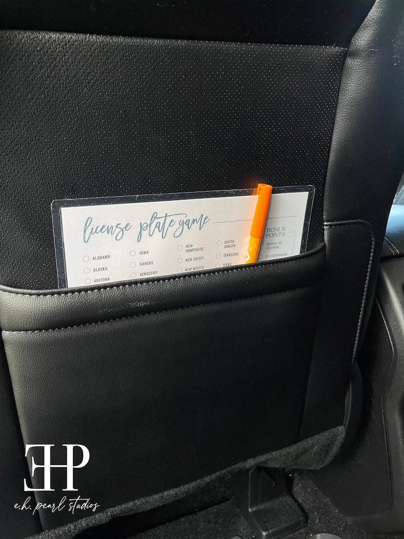 May include: A white card with the text "license plate game" printed on it. The card has a checklist of states with checkboxes next to each state name. A orange marker is placed on the card.