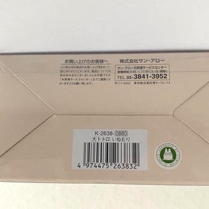 May include: A beige rectangular box with Japanese text and a barcode. The box has a clear plastic top and a green circular sticker with a cartoon character. The text includes a phone number and the words "大トトロ いねむり".