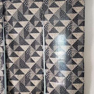 May include: Geometric patterned fabric curtains. The curtains feature a repeating triangle design in shades of black, gray, and beige. The fabric is hanging from a white curtain rod.