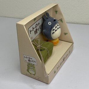 May include: A beige cardboard display box featuring a plush Totoro character and a small green gift box tied with twine. The box has Japanese text and a cartoon illustration of Totoro.