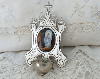 May include: Silver-toned metal religious wall decor featuring a small image of the Virgin Mary in a castle-like frame with a small cup below.