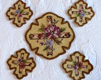 May include: Five embroidered cross-shaped needlepoint pieces with floral designs. The center piece is larger and features a cross with a large pink flower and smaller purple flowers. The four smaller pieces are identical and feature a cross with a smaller pink flower and purple flowers.