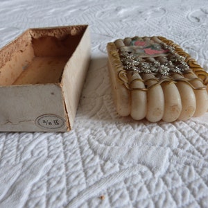 May include: A vintage box with a white label that says "3/8 T" and a white, cream-colored, and gold-trimmed decorative object inside.