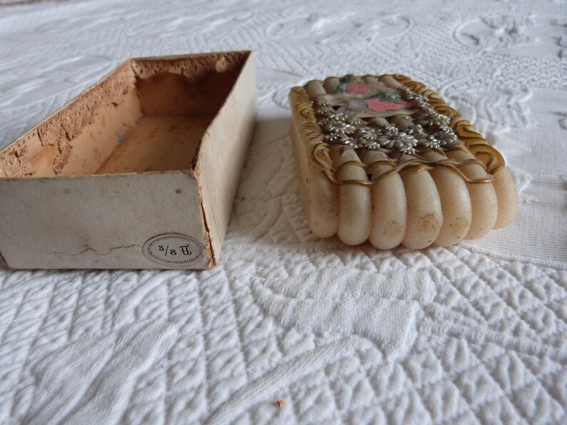 May include: A vintage box with a white label that says "3/8 T" and a white, cream-colored, and gold-trimmed decorative object inside.