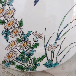 Pode incluir: Um prato de cer&acirc;mica branco com um design floral. O prato apresenta flores rosa e brancas com centros amarelos, folhas verdes e caules azuis. O design lembra um estilo japon&ecirc;s.