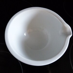 May include: A white ceramic bowl with a pouring spout. The bowl is empty and has a smooth, glossy finish.