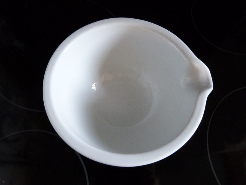 May include: A white ceramic bowl with a pouring spout. The bowl is empty and has a smooth, glossy finish.