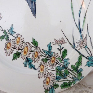 Pode incluir: Um prato de cer&acirc;mica branco com um design floral. O prato apresenta flores rosa e brancas com centros amarelos, folhas verdes e caules azuis. As flores est&atilde;o dispostas em um cacho no lado inferior direito do prato.