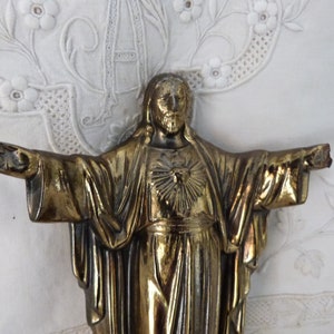 Op de afbeelding: Een gouden metalen beeld van Jezus Christus met zijn armen uitgestrekt. Het beeld toont Jezus met een hart op zijn borst.