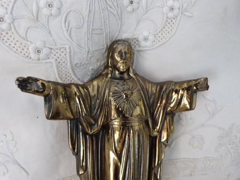 Op de afbeelding: Een gouden metalen beeld van Jezus Christus met zijn armen uitgestrekt. Het beeld toont Jezus met een hart op zijn borst.