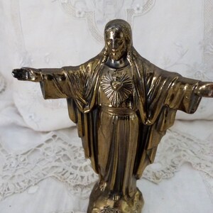 Op de afbeelding: Een gouden standbeeld van Jezus Christus met zijn armen uitgestrekt. Het standbeeld staat op een voetstuk en heeft een hart met een zonnestralenontwerp op zijn borst.