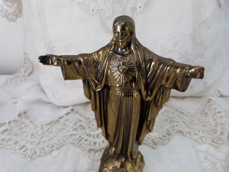Op de afbeelding: Een gouden standbeeld van Jezus Christus met zijn armen uitgestrekt. Het standbeeld staat op een voetstuk en heeft een hart met een zonnestralenontwerp op zijn borst.