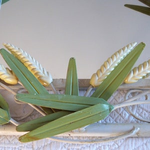May include: A white metal mirror with a decorative design of green leaves and yellow wheat stalks.