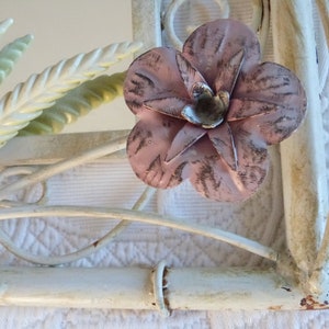 May include: White metal wall mirror with a pink flower and green leaves. The mirror has a decorative, ornate design.